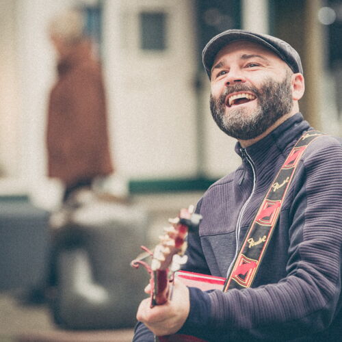 Rasmus Schumacher lacht beim Spielen seiner roten Akustikgitarre