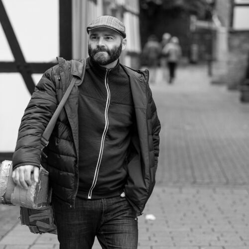 Schwarz-Weiß-Porträt von Rasmus Schumacher mit Gitarrenkoffer in einer Altstadt