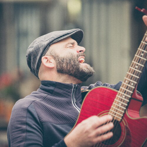 Rasmus Schumacher singt mit roter Akustikgitarre bei der Straßenmusik