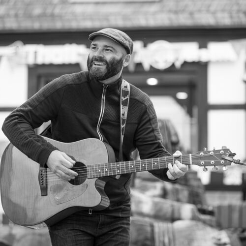 Rasmus Schumacher spielt Akustikgitarre auf einem Stadtplatz – Schwarz-Weiß