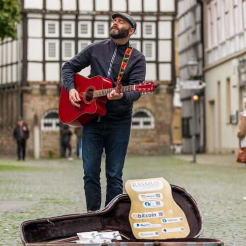 Rasmus Schumacher bei der Straßenmusik mit roter Gitarre und offenem Gitarrenkoffer
